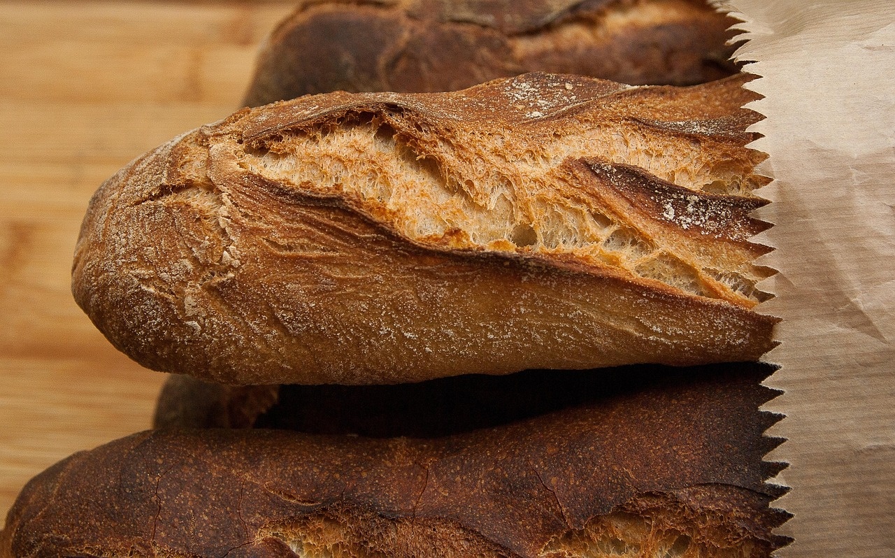 Baguette artigianale avvolta in carta da forno, crosta spezzata e dorata