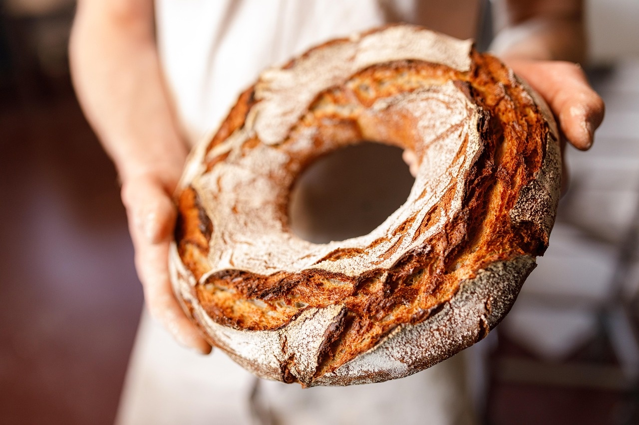 Mani del fornaio che sostengono una ciambella di pane rustico appena sfornata